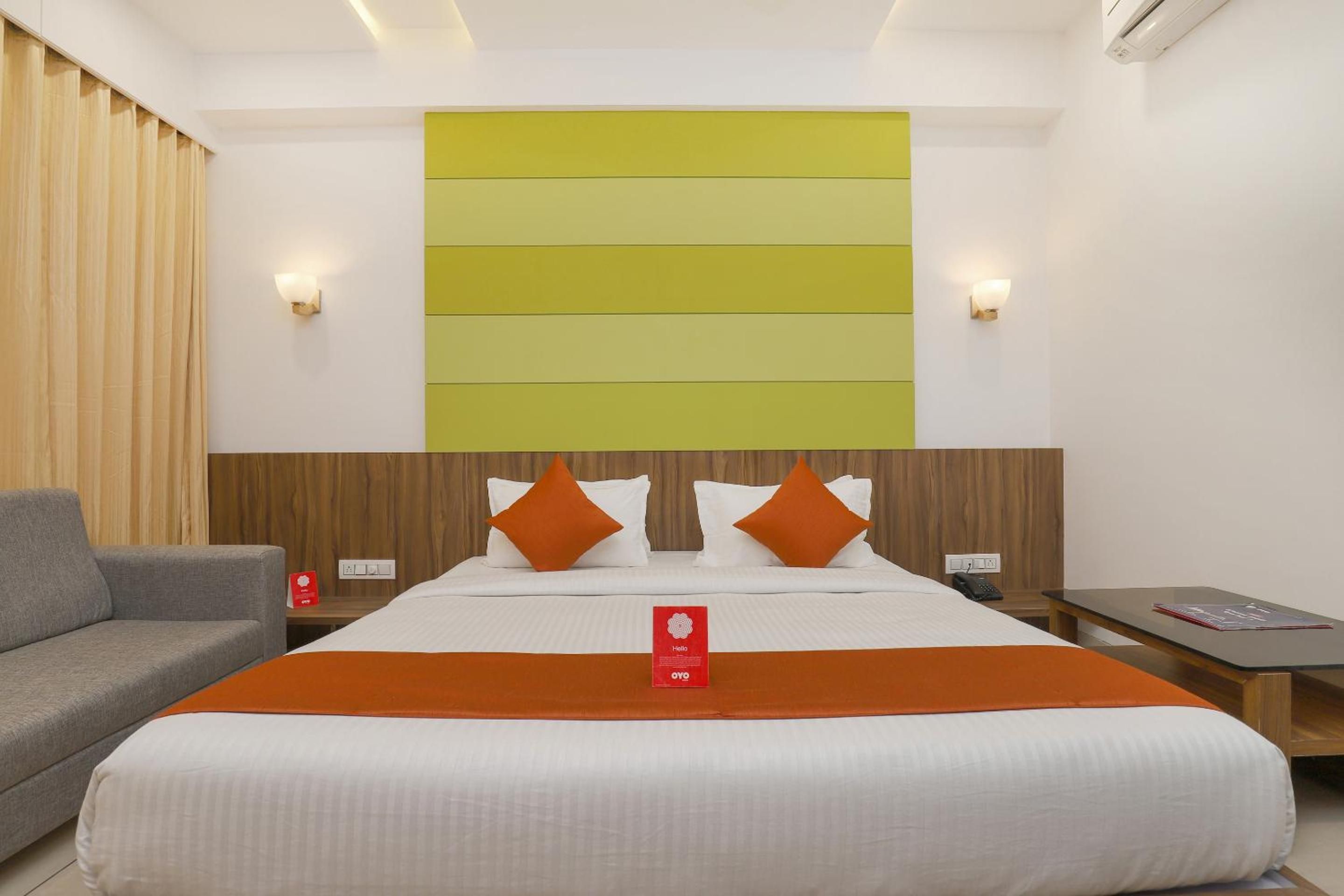 A hotel room with a large bed, a sofa, a nightstand, and a wall-mounted light fixture.