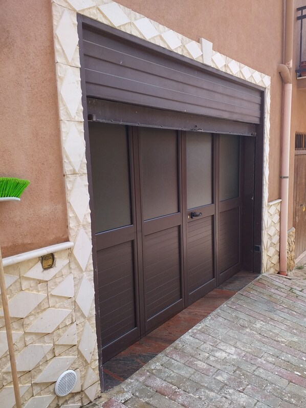A garage with a brown sliding door, stone wall, and a small green plant on the left.