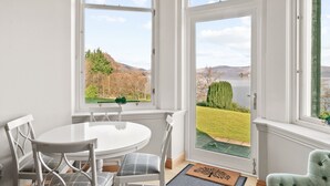 A dining area with a white table and chairs, large windows with a view of a lake and hills. - No 3 Lomond Castle - Sleeps 4 - sleeps 4 guests  in 2 bedrooms (ALEXANDRIA)