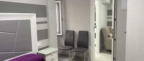 Ein Schlafzimmer mit einem Bett, einem Nachttisch, zwei Stühlen, einem Kleiderschrank und einer Tür zu einem anderen Raum.