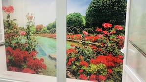 A window with a view of a garden featuring red flowers and a small pond. - Viana Rooms (Córdoba)