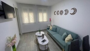 A modern living room with a teal sofa, a small round table, a green vase with flowers, and decorative wall art. - Viana Rooms (Córdoba)