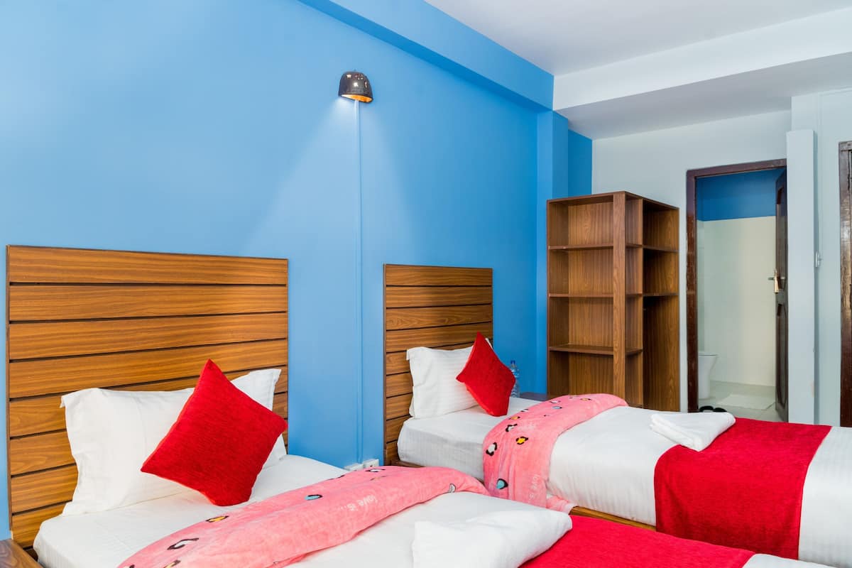 Une chambre d’hôtel avec deux lits, des têtes de lit en bois, des oreillers rouges, une couverture rose et une armoire en bois.