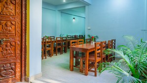 A dining area with wooden tables and chairs, a decorative wooden door, and potted plants. - Hotel Nepal Bhumi (Kathmandu)