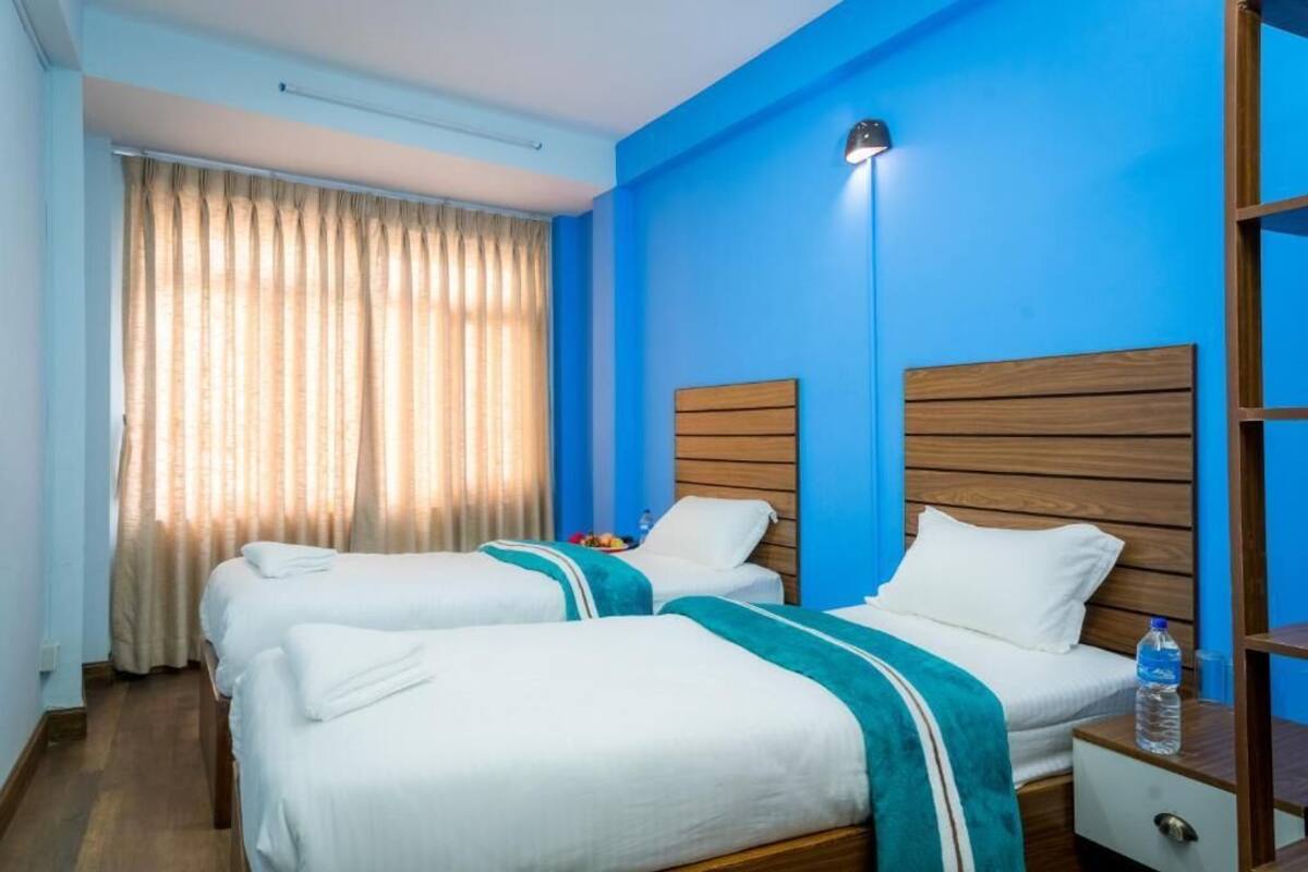 Une chambre d’hôtel avec deux lits, des têtes de lit en bois, une table de chevet et une fenêtre avec des rideaux.