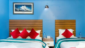 Habitación de hotel con dos camas, cada una con almohadas rojas y blancas, un cuadro enmarcado de una montaña en la pared, y una mesita de noche con una botella de agua y un teléfono.