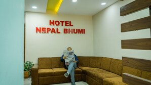 A man sitting on a brown sofa in a hotel lobby with a sign reading "HOTEL NEPAL BHUMI" on the wall. - Hotel Nepal Bhumi (Kathmandu)