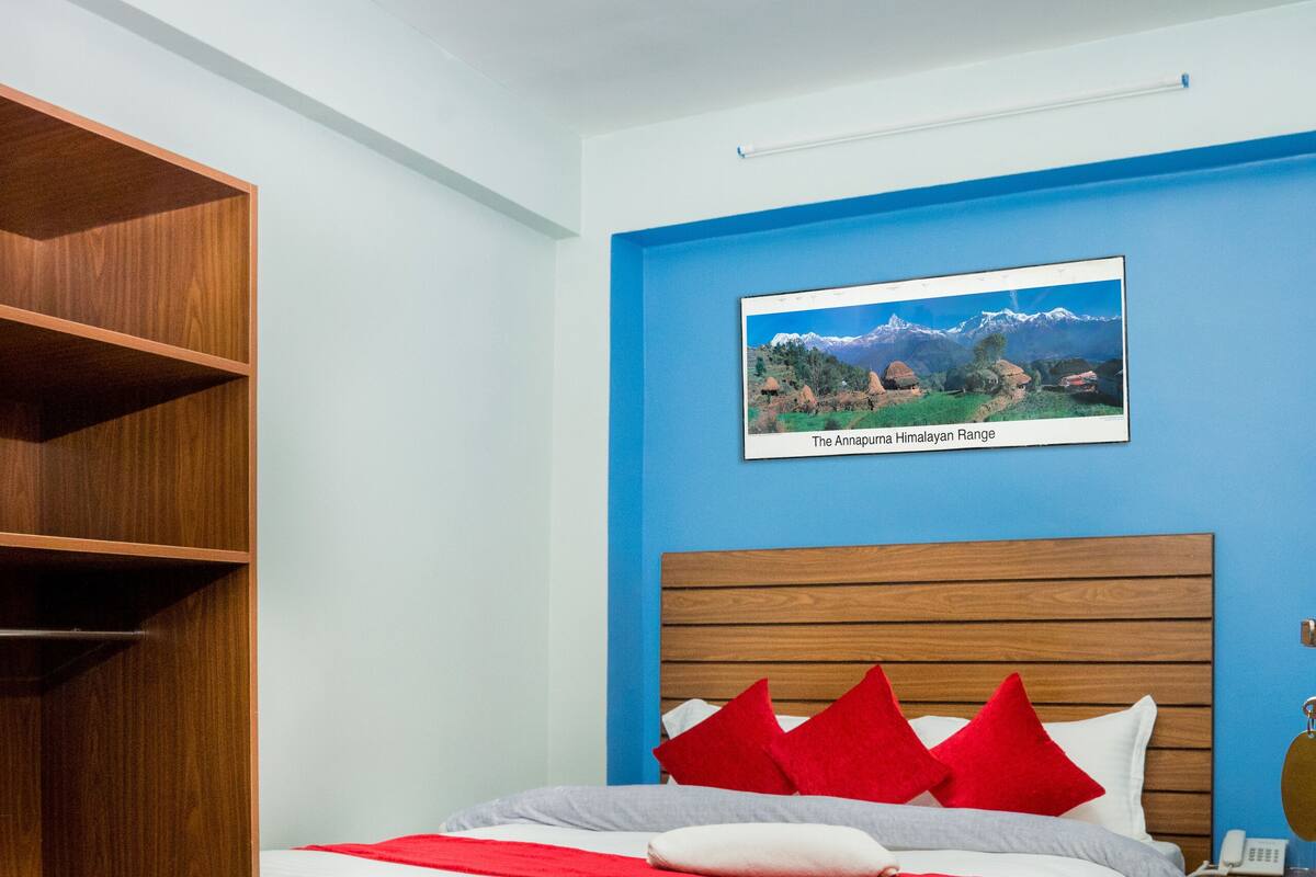 Une chambre à coucher avec un lit en bois, une literie rouge et blanche, un mur bleu et un tableau encadré représentant une chaîne de montagnes.