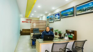 A hotel reception desk with a receptionist, a laptop, framed pictures on the wall, and a sign indicating the hotel name. - Hotel Nepal Bhumi (Kathmandu)
