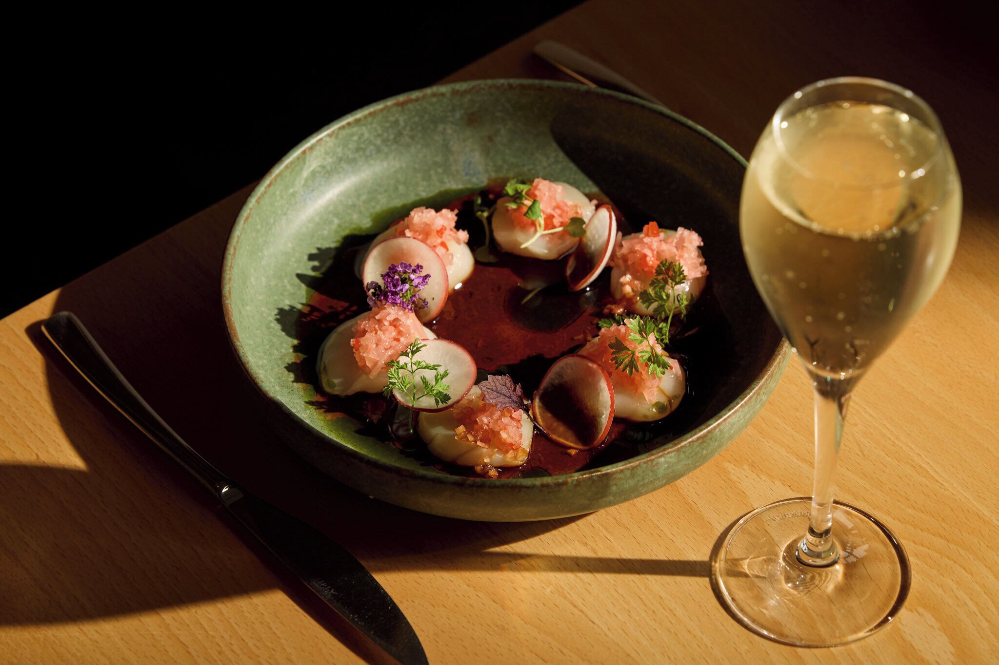 A plate of food with a glass of white wine on a wooden table.