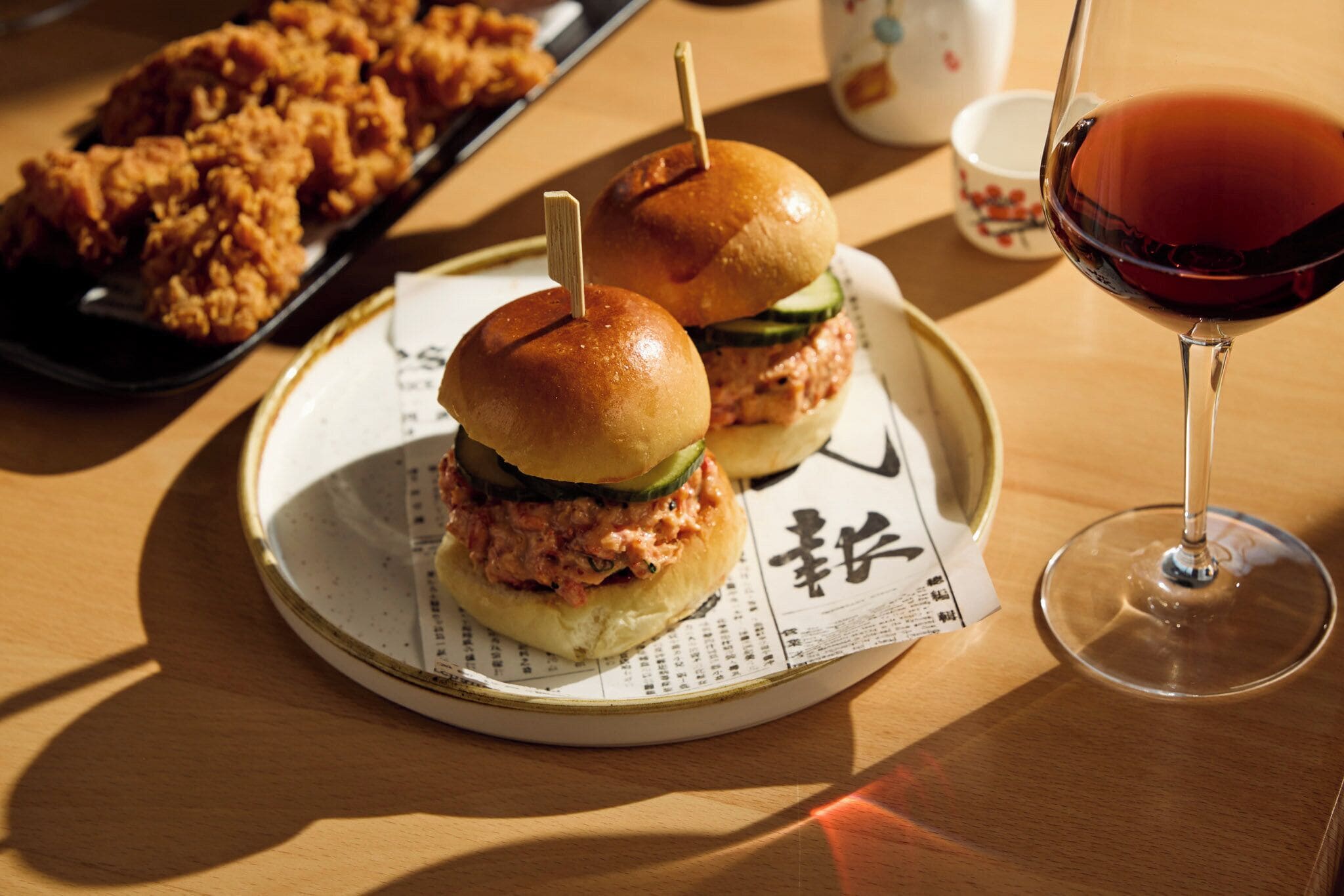 A plate with two sandwiches, a glass of red wine, and a tray of fried chicken.