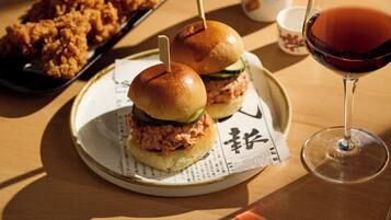 A plate with two sandwiches, a glass of red wine, and a tray of fried chicken.