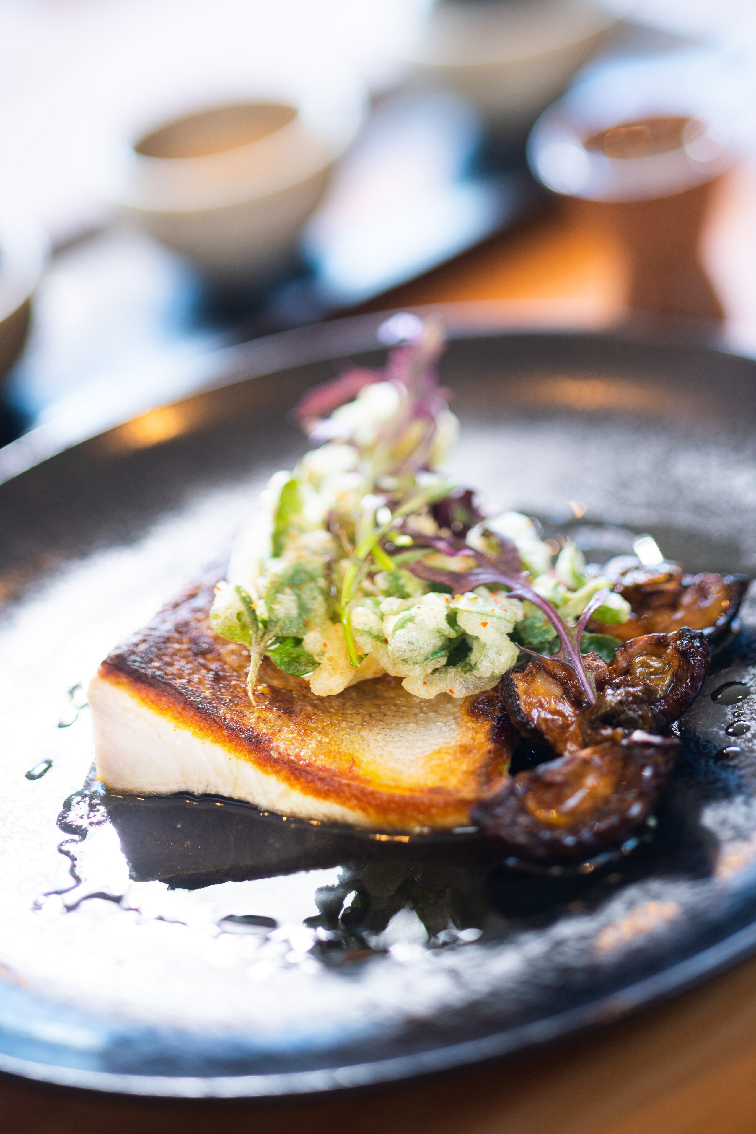 A plate with a piece of fish, greens, and mushrooms.