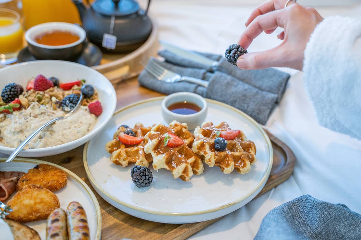 Une table dressée pour le petit-déjeuner avec des gaufres, des fruits rouges et des saucisses sur des assiettes.
