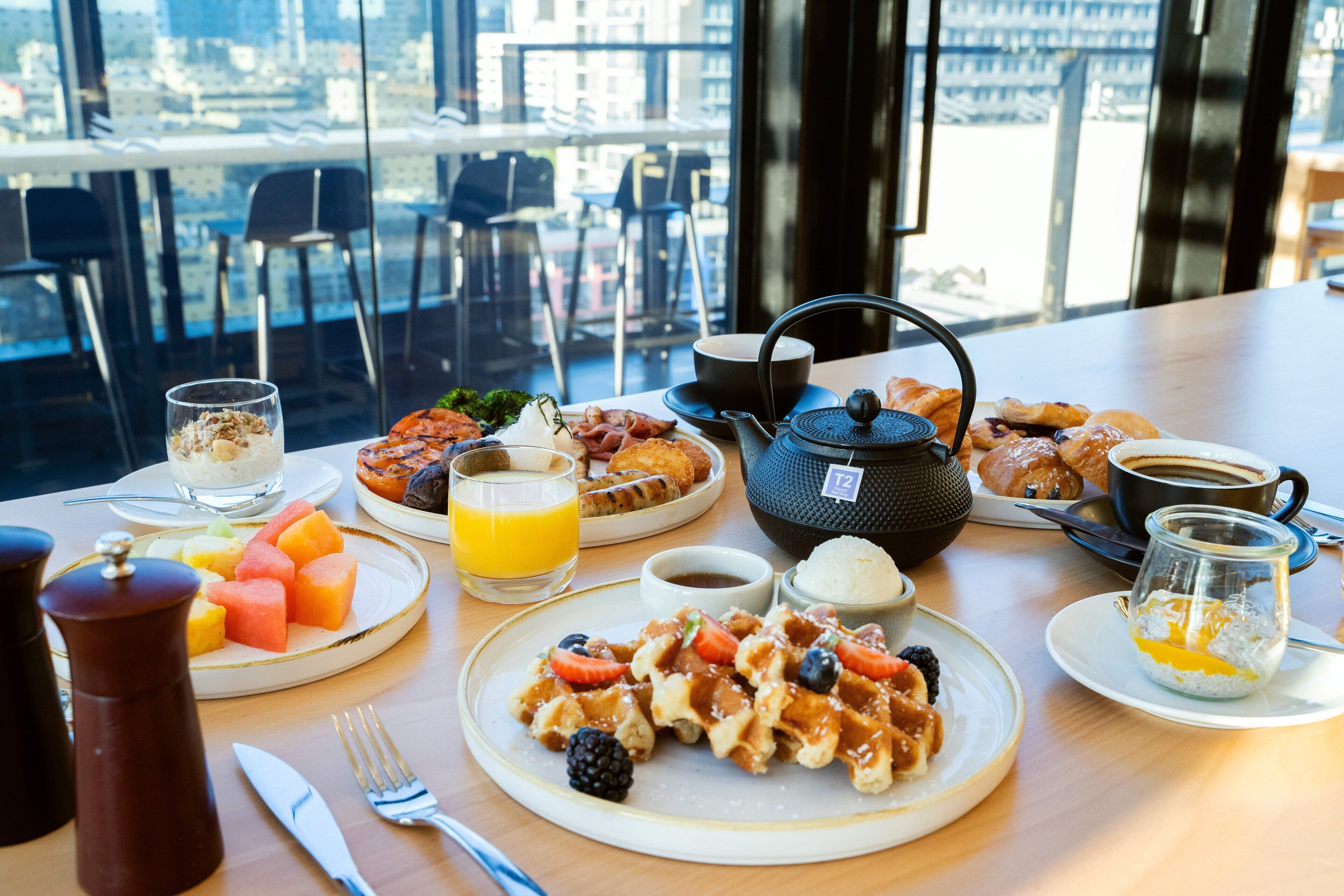 Uma mesa de café da manhã com waffles, frutas, café e doces.