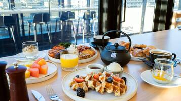 Uma mesa de café da manhã com waffles, frutas, café e doces.