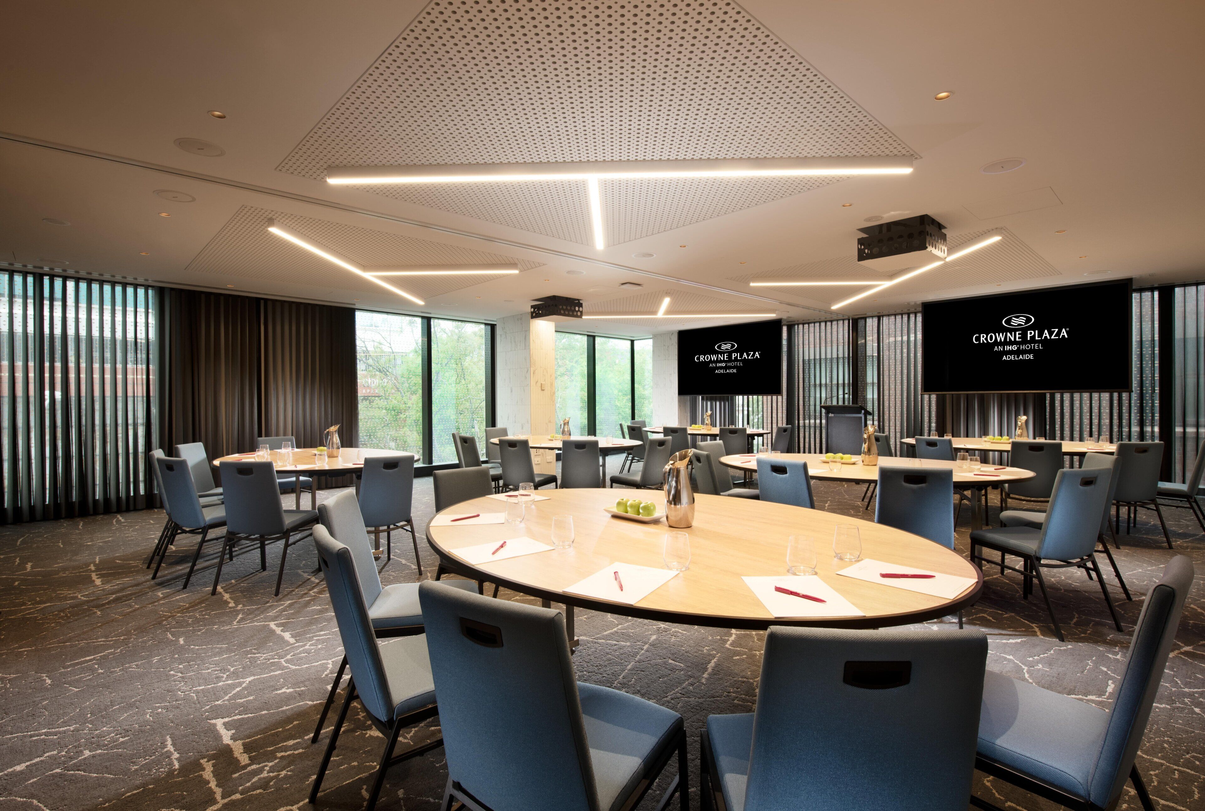 A conference room with round tables, chairs, and a large screen displaying the hotel's name.