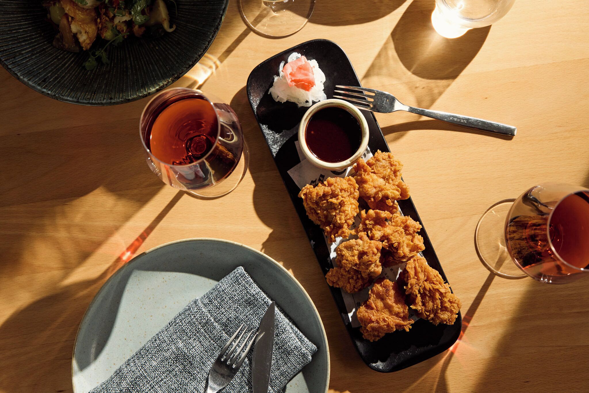 A dining table with a black plate of fried chicken, a small bowl of sauce, and a glass of tea.