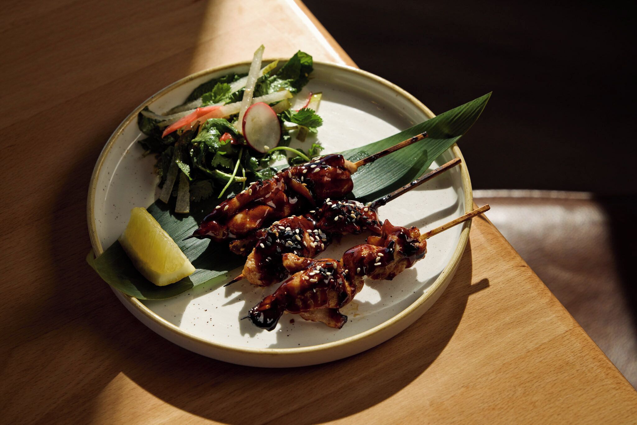 A plate with skewered meat, a salad, and a lemon wedge.