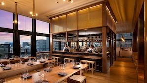 Een moderne bar met een hoge plafond, grote ramen en stadszicht.