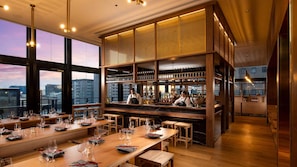 Eine moderne Bar mit hoher Decke, großen Fenstern und Blick auf die Stadt.