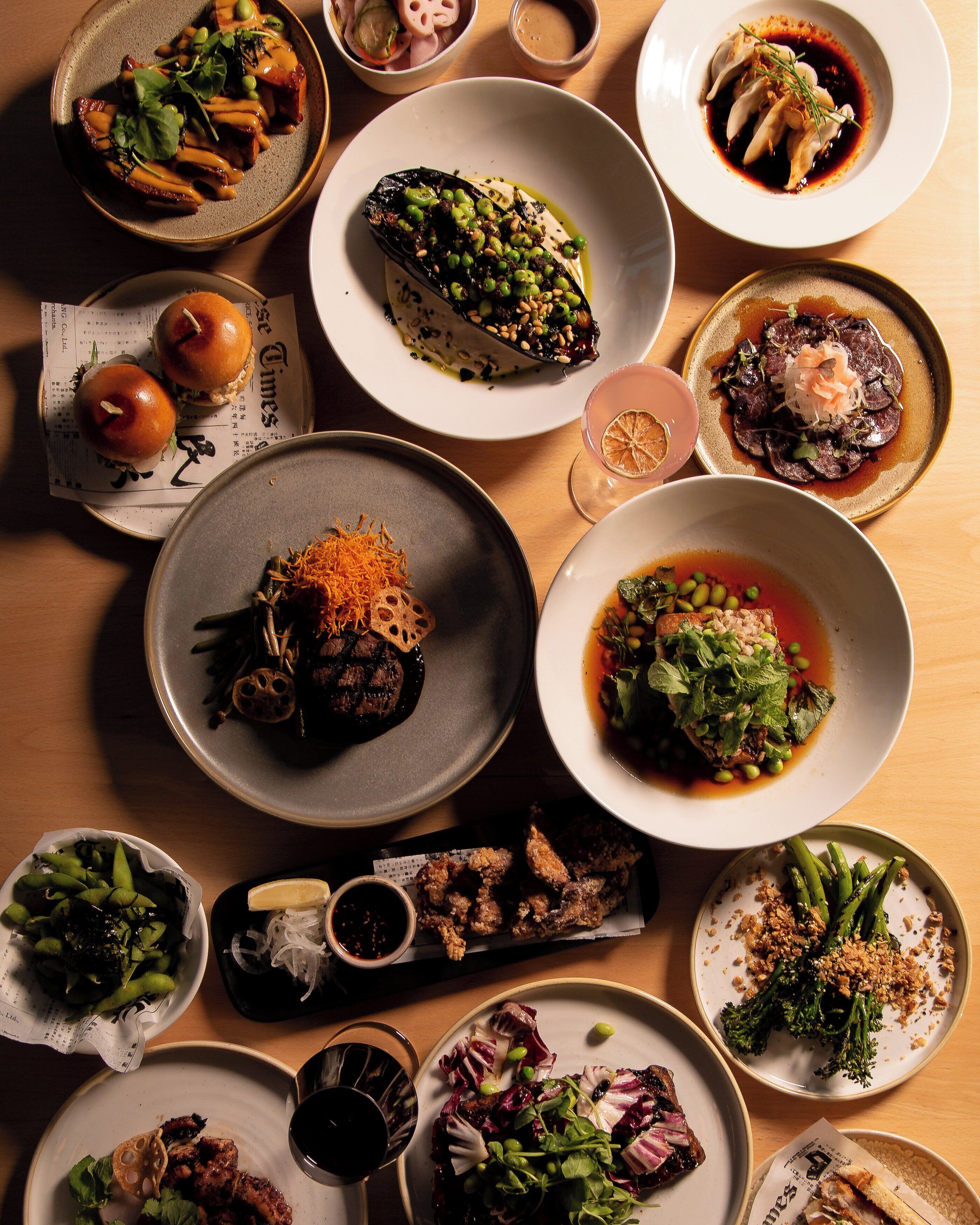 A variety of dishes on a wooden table, including sushi, dumplings, and a bowl of soup.