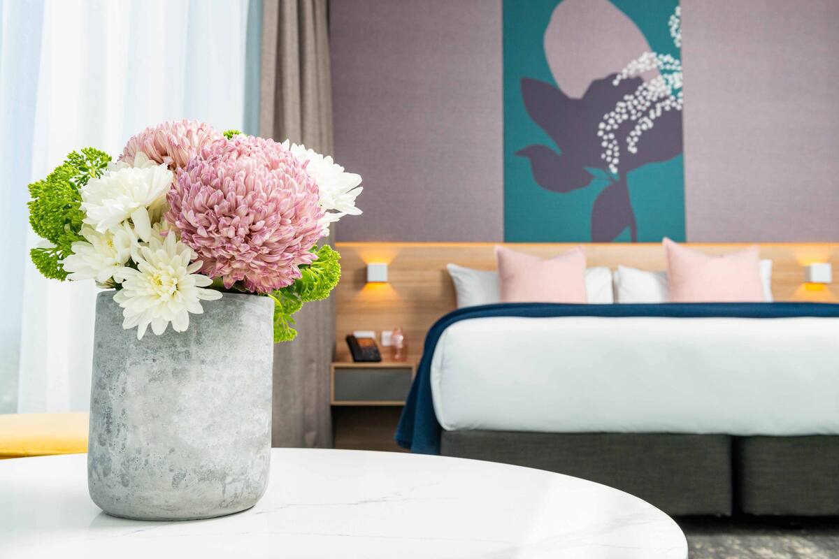 Une chambre d’hôtel avec un lit, une table de chevet et un vase de fleurs posé sur une table ronde.