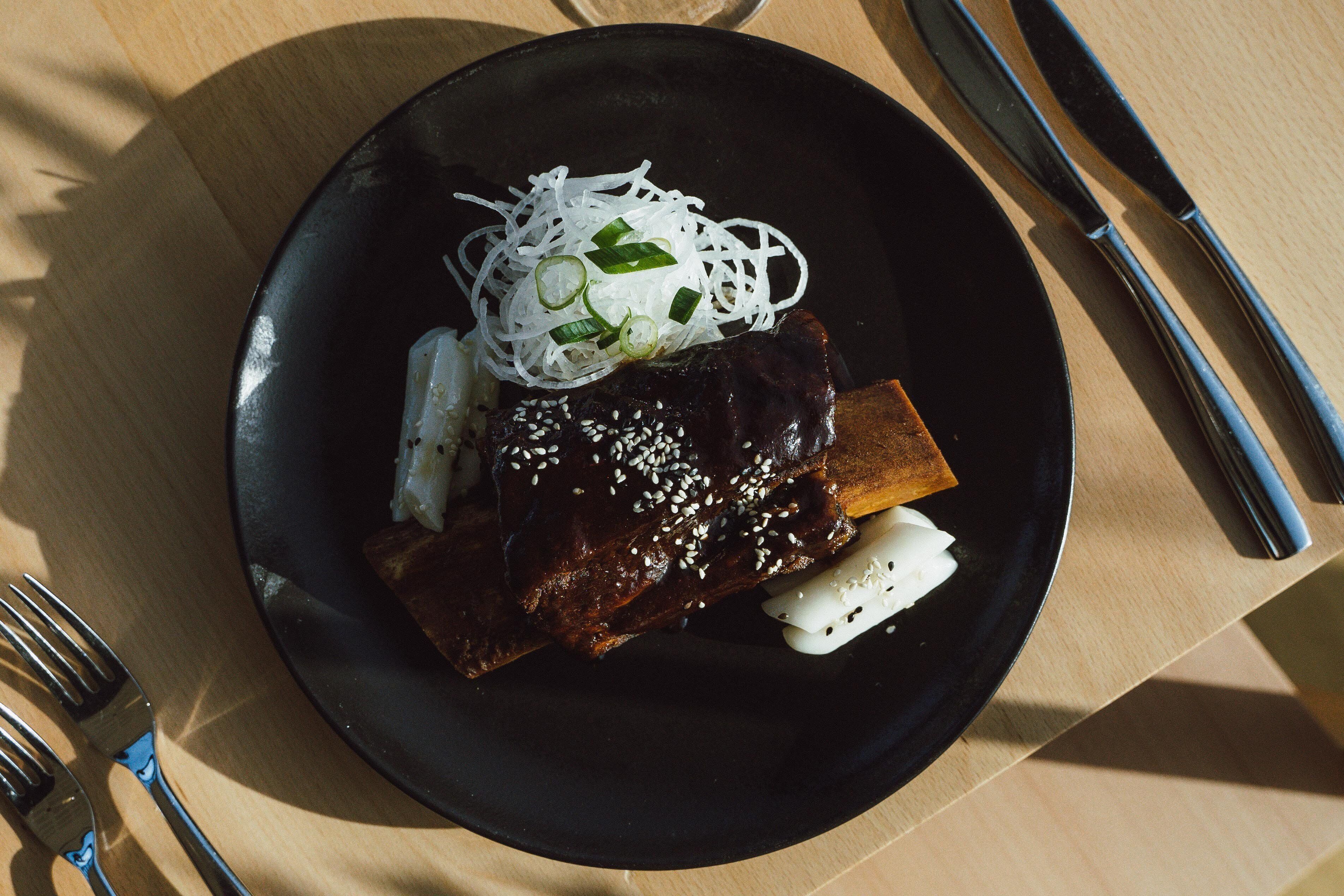 A plate with ribs and noodles on a black plate.