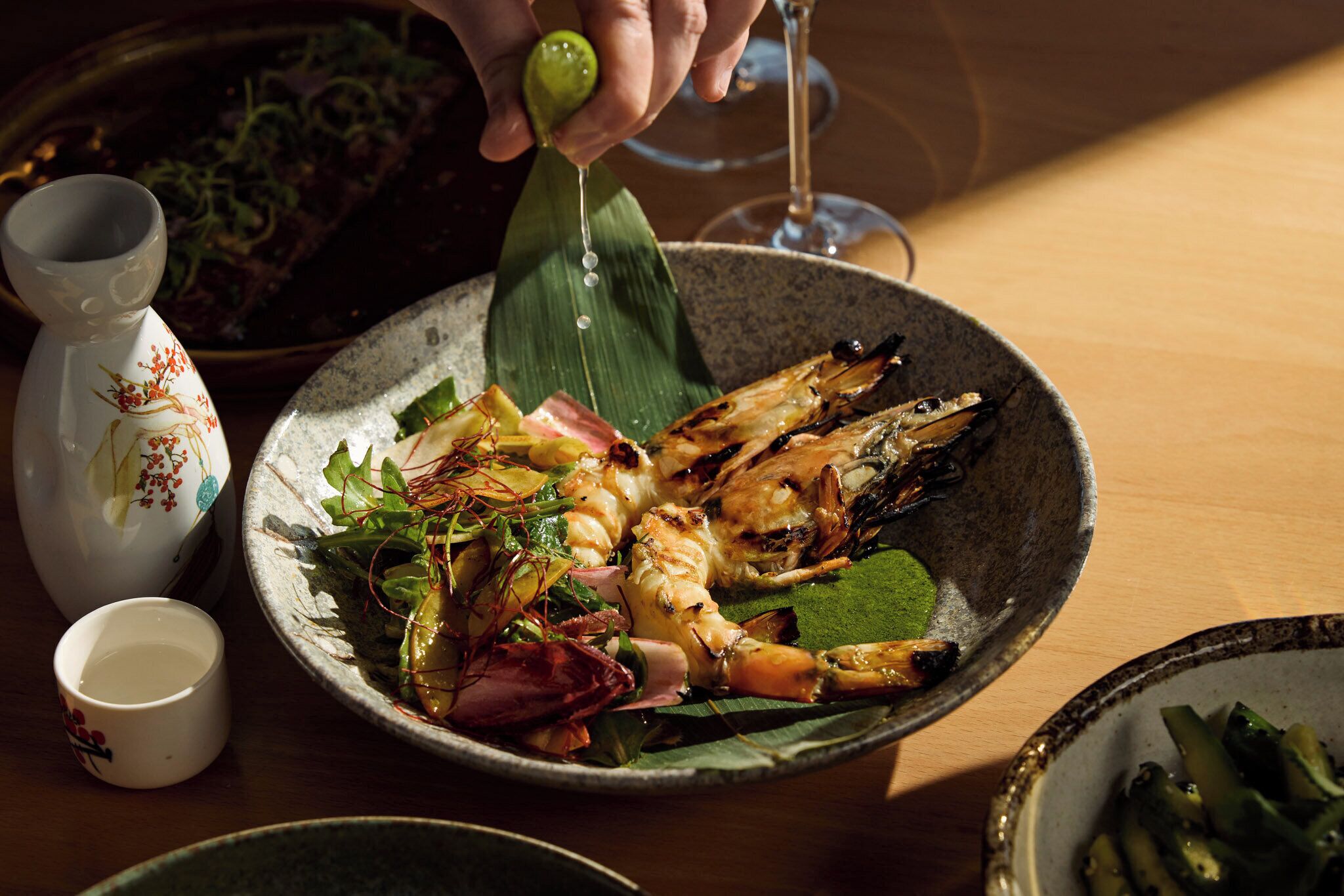 A dining table with a bowl of grilled seafood, a small bowl of sauce, and a decorative vase.