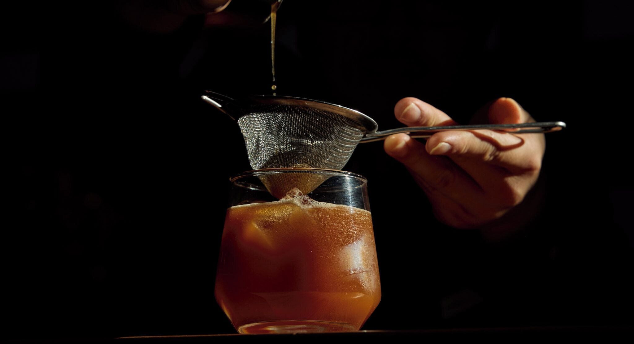 Una persona vertiendo un líquido en un vaso con un colador de metal.
