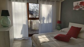 Une chambre à coucher avec un lit, une table de chevet, une lampe et une vue sur l’extérieur par une porte.