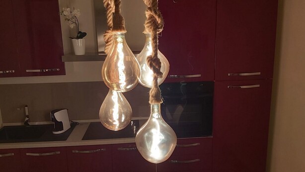 Ett kök med röda skåp, en vit bänkskiva och en hängande lampa som består av två glödlampor i glas, upphängda i ett rep.