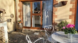 Une terrasse avec une table et des chaises en métal, une plante en pot et un mur en briques.
