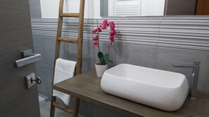 Une salle de bain avec un banc en bois, un lavabo blanc, une orchidée en pot et une serviette accrochée au mur.