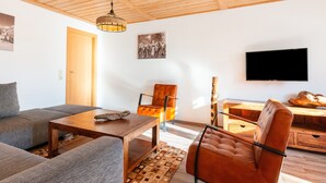 Ein modernes Wohnzimmer mit Holzboden, einer Couch, einem Couchtisch, einem Ledersessel und einem flachbildfernseher an der Wand.