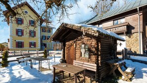 Eine Holzhütte mit einer Bank und einem Tisch in verschneiter Landschaft.