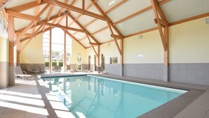 A large indoor swimming pool with a high ceiling and wooden beams, surrounded by lounge chairs and a view of the outdoors. - Holiday Home in Ardennes With Pool & Sauna (Rendeux)
