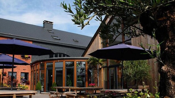 An outdoor patio area with wooden benches and tables, surrounded by plants and flowers. - Holiday Home in Ardennes With Pool & Sauna (Rendeux)