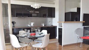 A modern kitchen with black cabinets, a dining area with a glass table, white chairs, and a red chair. - 1-Br Apartment, Sea View, Steps from Beaches (Cannes)