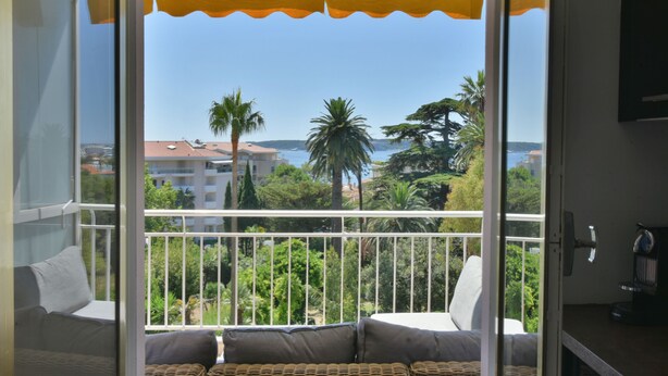 A balcony with wicker furniture, a view of the sea, and buildings in the background. - 1-Br Apartment, Sea View, Steps from Beaches (Cannes)