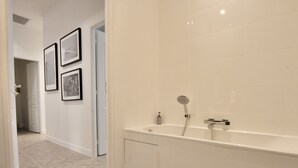 A modern bathroom with a freestanding bathtub, white tiled walls, and a herringbone floor pattern. - Modern 3-Br Apartment in City Center, 5 Minutes from Palais and Beache (Cannes)
