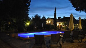 An outdoor swimming pool area with lounge chairs and umbrellas, surrounded by trees and a building in the background. - Casa del Riu (Beneixama)