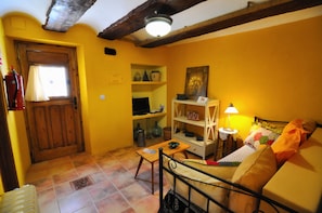 A cozy living room with a wooden door, a sofa, a table, and shelves with various items.