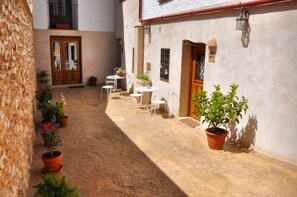 A courtyard with potted plants, white chairs, and a door leading to a room.