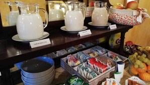 A buffet setup with pitchers of milk, a bowl of apples, and various packaged snacks. - Casa del Riu (Beneixama)