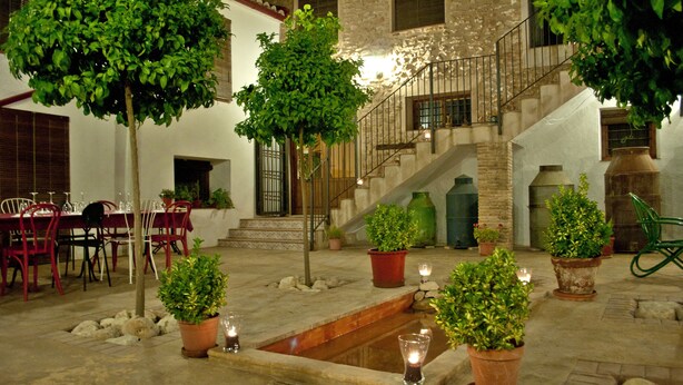 An indoor courtyard with a dining area, potted plants, a small water feature, and a staircase. - Casa del Riu (Beneixama)