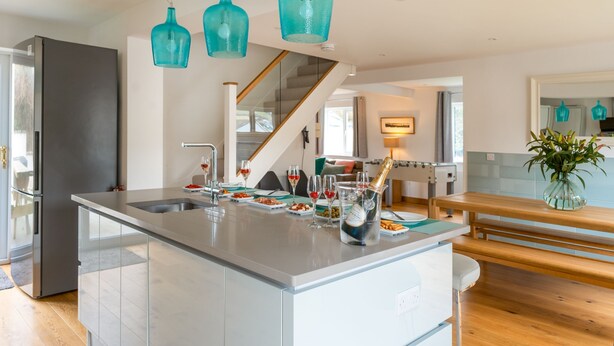 Una cocina moderna con una isla central, electrodomésticos de acero inoxidable e iluminación colgante color turquesa.