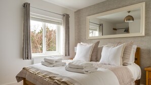 Una cama bien hecha con toallas dobladas, un espejo grande y un ventanal con cortinas.