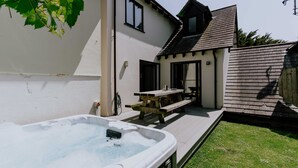 Un patio trasero con jacuzzi, terraza de madera, mesa de picnic y una casa con techo inclinado.