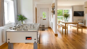 Una habitación moderna con mesa de futbolín, una mesa de comedor con bancos, un televisor montado en la pared y un ventanal con vistas a la vegetación.